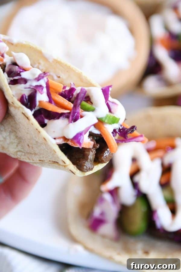 Game Changing Korean Beef Tacos with Zesty Slaw and a Sauce Beyond Compare 4 Hand holding a single Korean beef taco, showcasing the layers of tender beef, crunchy slaw, and drizzled sauce.
