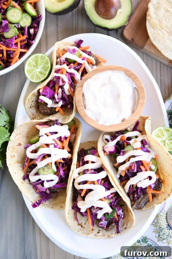 Game Changing Korean Beef Tacos with Zesty Slaw and a Sauce Beyond Compare 5 Top-down view of four Korean beef tacos, artfully arranged with vibrant slaw and generous drizzles of the signature sauce on a white platter.