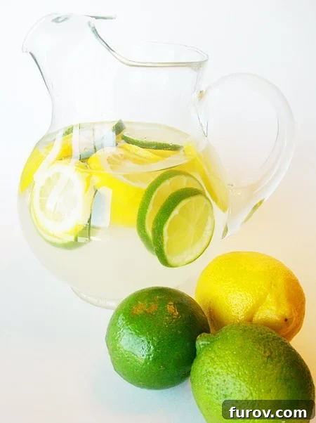 Glass pitcher with clear punch and lemon and lime slices, ready to be served for a refreshing experience.