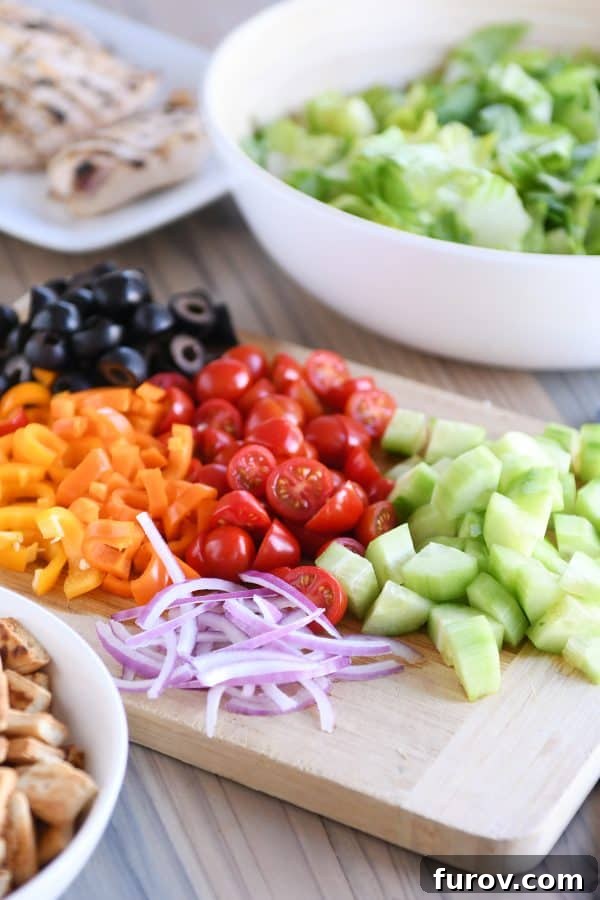Effortless Entertaining Build Your Own Meals For Any Crowd Recipes and Tips 4 A wooden cutting board laden with freshly chopped cucumbers, juicy tomatoes, colorful bell peppers, and briny olives, ready for a build-your-own meal.