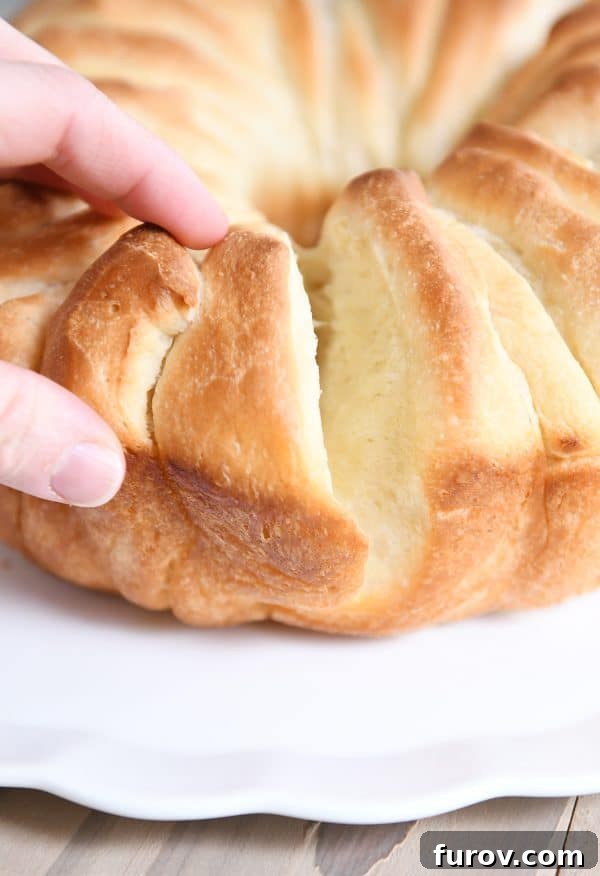 Someone pulling off a piece of a loaf of buttery bundt bread, showcasing its fluffy texture and golden crust.