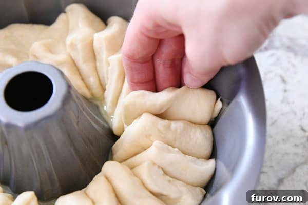 Another perspective on layering squares of dough in a bundt pan, highlighting the neat and organized placement of each piece.