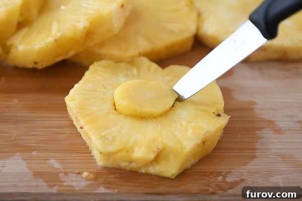 Cutting out the fibrous core of a fresh pineapple slice with a round cookie cutter.