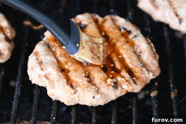 Brushing a grilled turkey burger generously with rich teriyaki sauce.