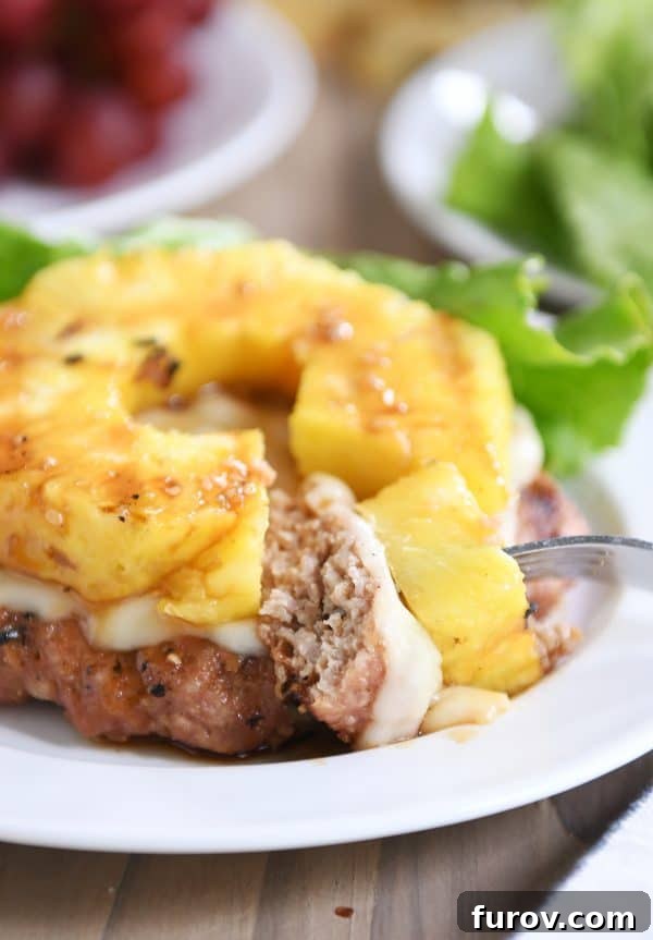 A close-up of a teriyaki turkey burger with a bite taken out, showing the grilled pineapple and melted Swiss cheese without a bun.