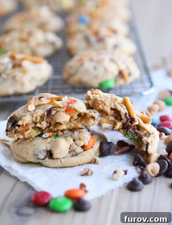 Sweet and Salty Peanut Butter Kitchen Sink Cookies 2 Baked peanut butter kitchen sink cookies with one broken in half, showcasing its rich texture and diverse inclusions.