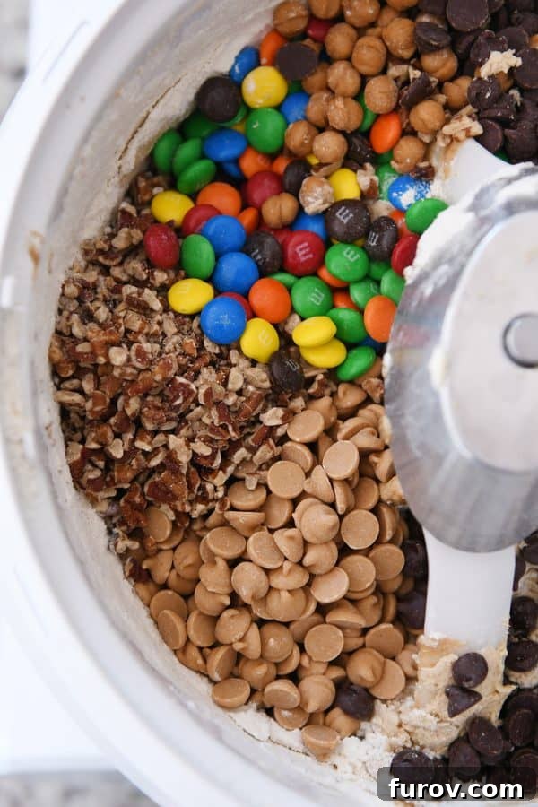 Sweet and Salty Peanut Butter Kitchen Sink Cookies 5 A bowl of rich peanut butter cookie dough overflowing with chocolate chips, peanut butter chips, caramels, M&M's, and pecans, ready to be mixed.