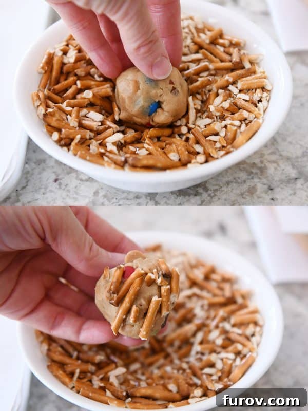 Sweet and Salty Peanut Butter Kitchen Sink Cookies 7 Hands pressing crushed pretzels onto an unbaked peanut butter kitchen sink cookie dough ball, creating a rustic, textured surface.
