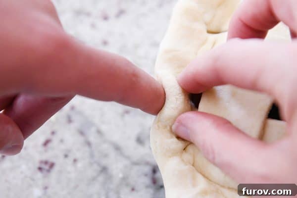 Detail shot of hands fluting the edge of a cherry pie crust, creating a decorative border.