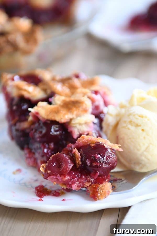 A fork holding a bite-sized piece of cherry pie, showing the flaky crust and juicy filling.
