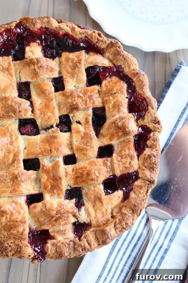 A whole baked cherry pie with a golden, intricately woven lattice crust, sitting on a wire rack.