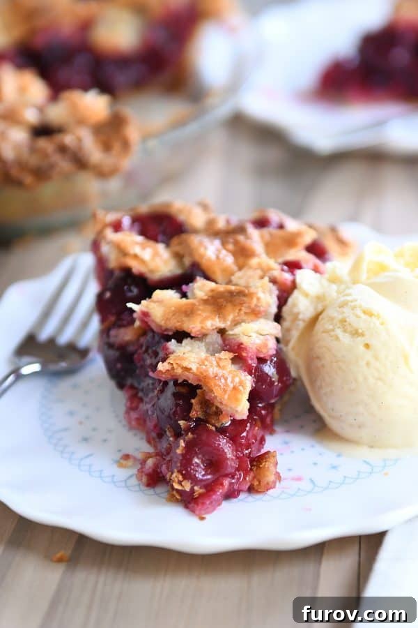 A slice of warm cherry pie on a white plate, served with a generous scoop of creamy vanilla ice cream.