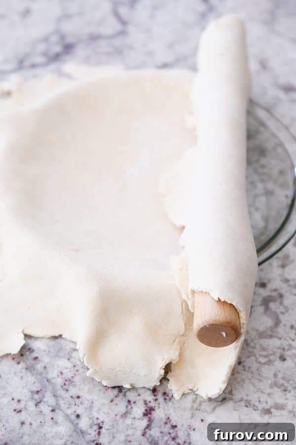 Rolling out a pie crust and gently placing it into a 9-inch glass pie plate, preparing the base for the cherry pie.