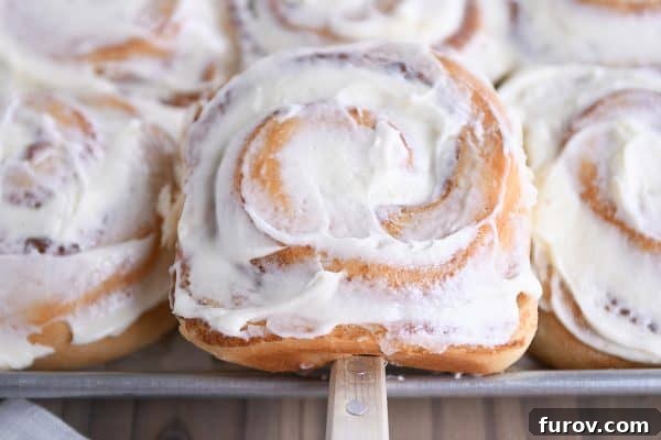 A spatula lifting out a perfectly frosted cinnamon roll from a half sheet pan, inviting and delicious.
