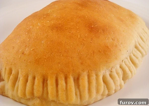 A freshly baked golden-brown Philly Cheesesteak Calzone resting on a white plate, showcasing its crispy texture.