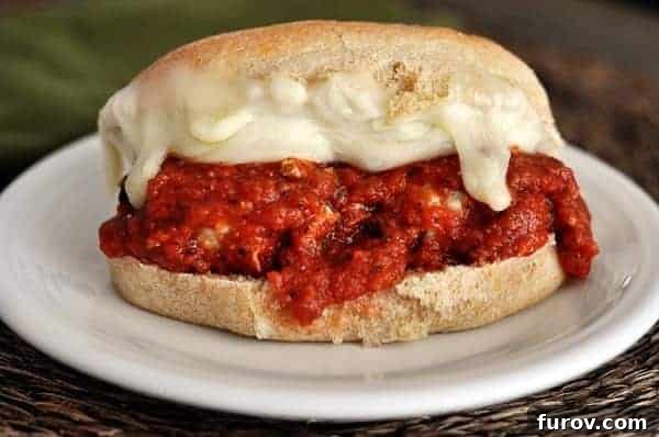 A perfectly assembled Italian meatball and cheese sub sandwich on a pristine white plate, showcasing melted cheese and rich tomato sauce.