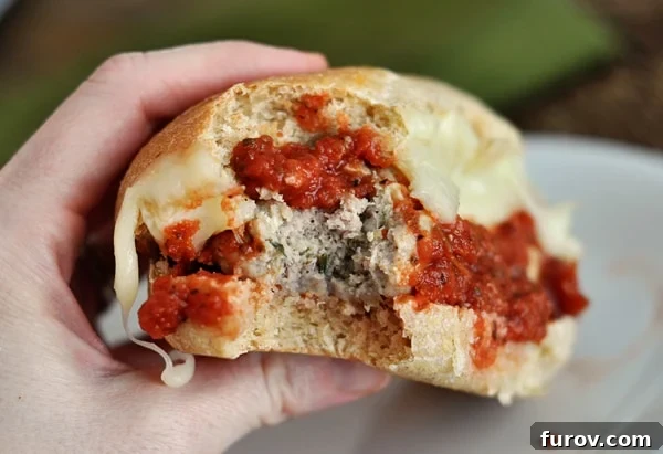 A close-up view of an Italian meatball and cheese sub sandwich with a bite taken out, revealing the succulent meatball and melted cheese.