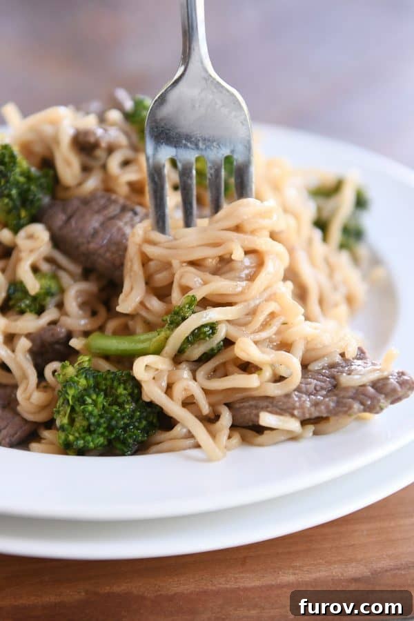 Effortless Beef and Broccoli Ramen Skillet 3 Twisting ramen noodles on fork with beef and broccoli on white plate. A close-up of flavorful beef and broccoli ramen noodles.