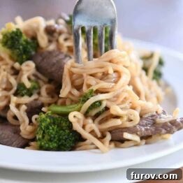 Twisting ramen noodles on fork with beef and broccoli on white plate.