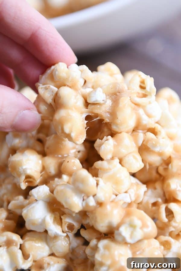 Gooey Peanut Butter Popcorn 3 A close-up shot of a hand gently pulling off a piece of the delectable peanut butter caramel popcorn, highlighting its irresistible chewiness.