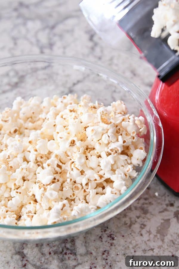 Gooey Peanut Butter Popcorn 5 An air popper expertly popping fresh popcorn kernels directly into a large glass bowl, creating a fluffy foundation for the peanut butter caramel.