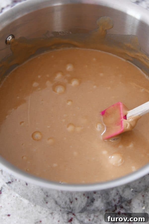 Gooey Peanut Butter Popcorn 8 The peanut butter caramel mixture in the saucepan, perfectly stirred until smooth and creamy, boasting an enticing golden-brown hue.