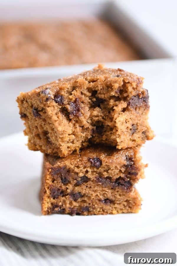 Two pieces of pumpkin chocolate chip snack cake stacked with a bite taken out, showcasing its moist texture and chocolate chips.