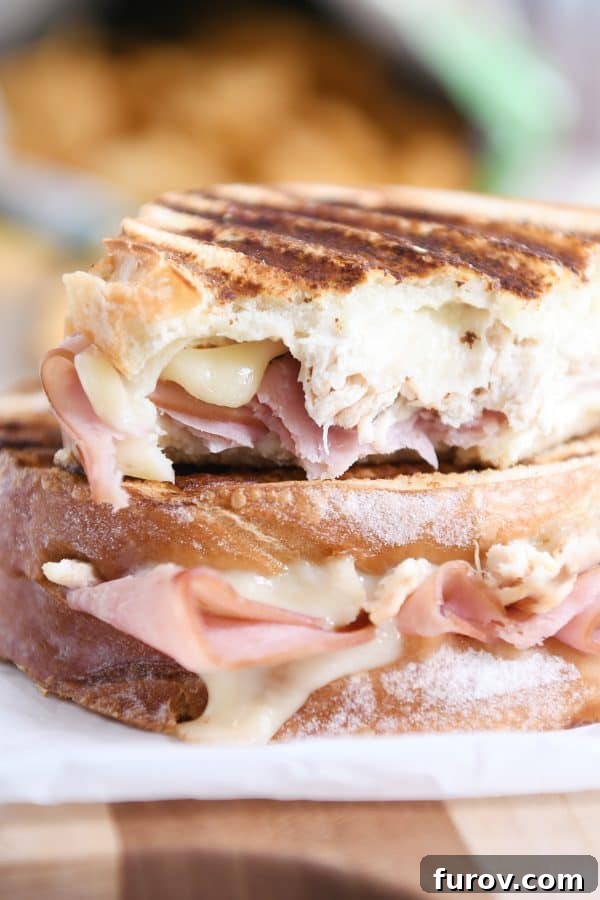 Close-up of a Chicken Cordon Bleu Panini with a bite taken, revealing melted Swiss cheese, tender chicken, and savory ham.