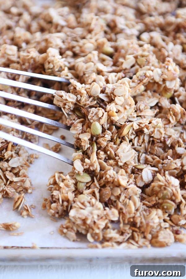 Sheet pan with parchment and spatula sliding granola into a pile.