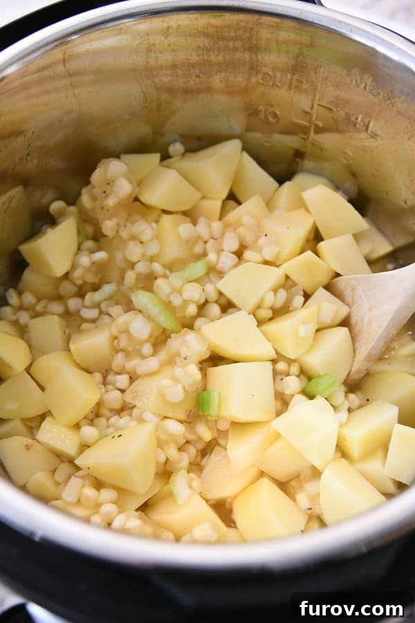 A top-down view inside an Instant Pot, showing diced potatoes and vibrant corn kernels as the base layers of the chowder.
