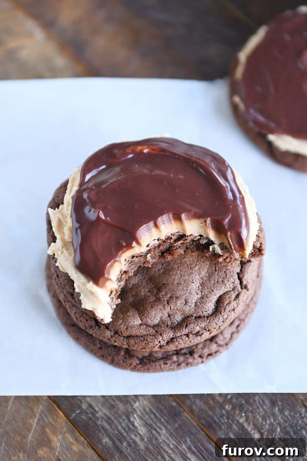Stack of chocolate peanut butter buckeye cookies with a delicious bite taken out, revealing layers of cookie, frosting, and ganache.