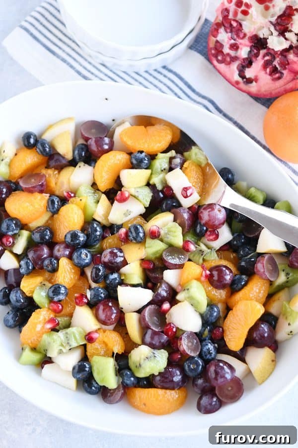 Top down view of white bowl with grapes, blueberries, pears, kiwi, oranges and pomegranate seeds for easy winter fresh fruit salad.