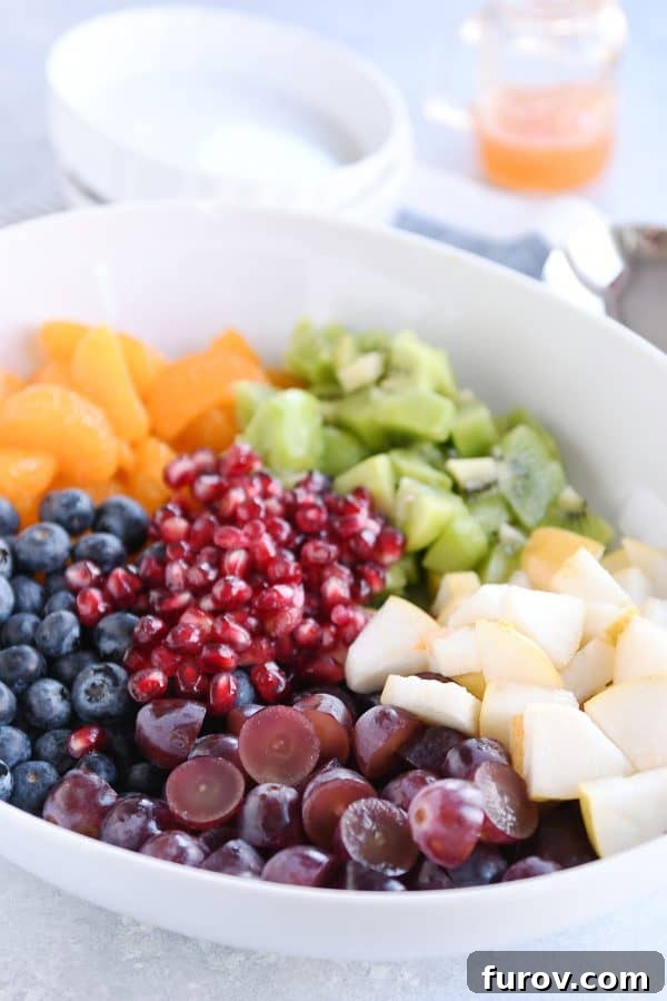 White bowl with grapes, blueberries, pears, kiwi, oranges and pomegranate seeds for easy winter fresh fruit salad.