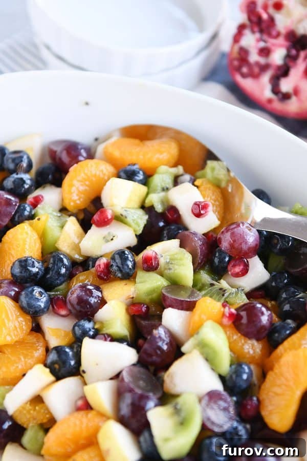 White bowl and spoon with grapes, blueberries, pears, kiwi, oranges and pomegranate seeds for easy winter fresh fruit salad.