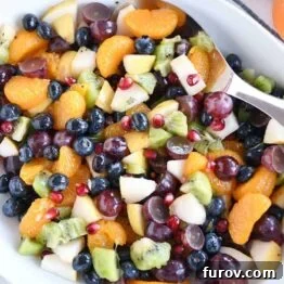 Top down view of white bowl with grapes, blueberries, pears, kiwi, oranges and pomegranate seeds for easy winter fresh fruit salad.