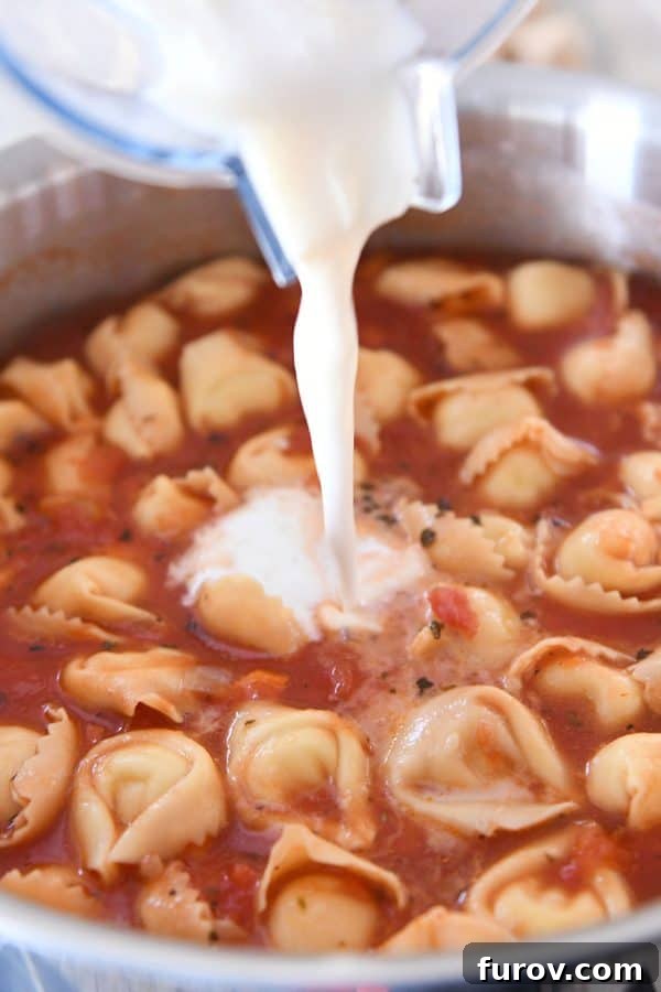 A hand pours a smooth milk and flour mixture into the simmering Tuscan tortellini soup, initiating the creaming process without heavy cream.