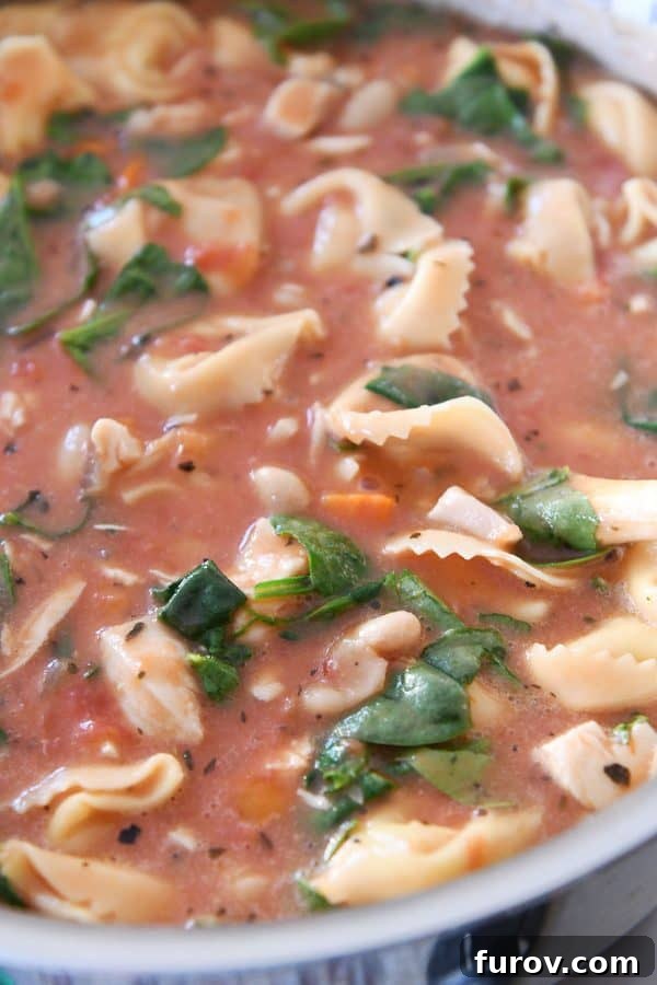 The creamy Tuscan tortellini soup gently simmers in a large pot on the stovetop, its rich aroma filling the kitchen as it finishes cooking.