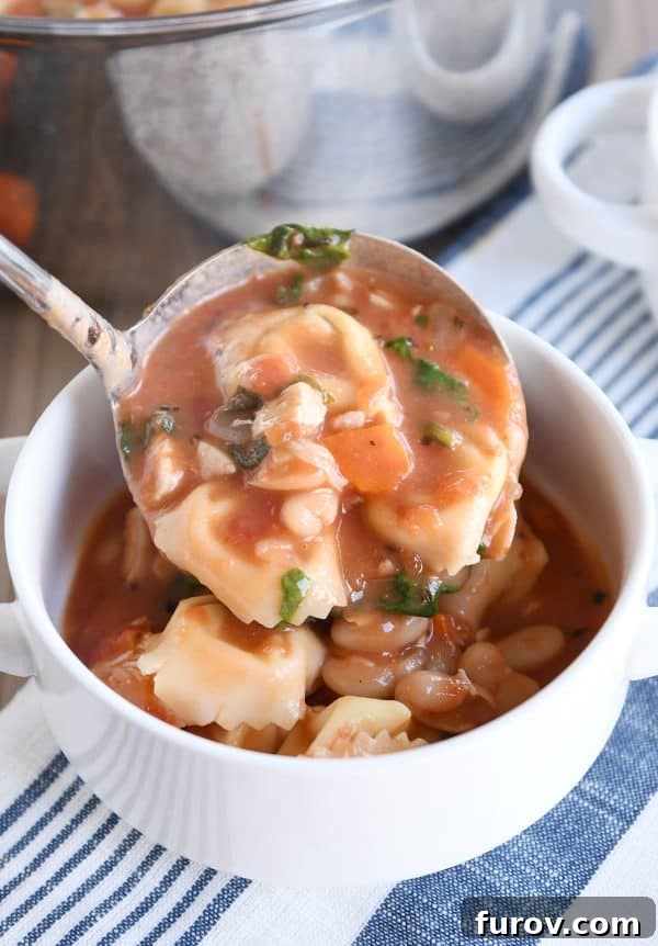 A ladle carefully pours a serving of creamy Tuscan tortellini soup into a pristine white bowl, ready to be enjoyed.