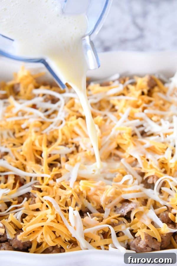 Pouring the whisked egg, milk, and sour cream mixture over the layered tater tot breakfast casserole ingredients.