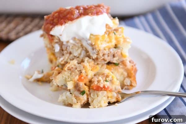 Two squares of tater tot breakfast casserole stacked on a white plate, garnished with sour cream and salsa, with a fork taking a bite.