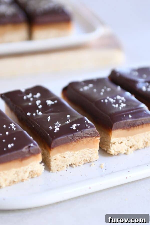 Homemade Dulce de Leche Caramel Shortbread Bars 2 Sliced homemade grown up Twix bars on white tray, showcasing the layers of shortbread, caramel, and chocolate.