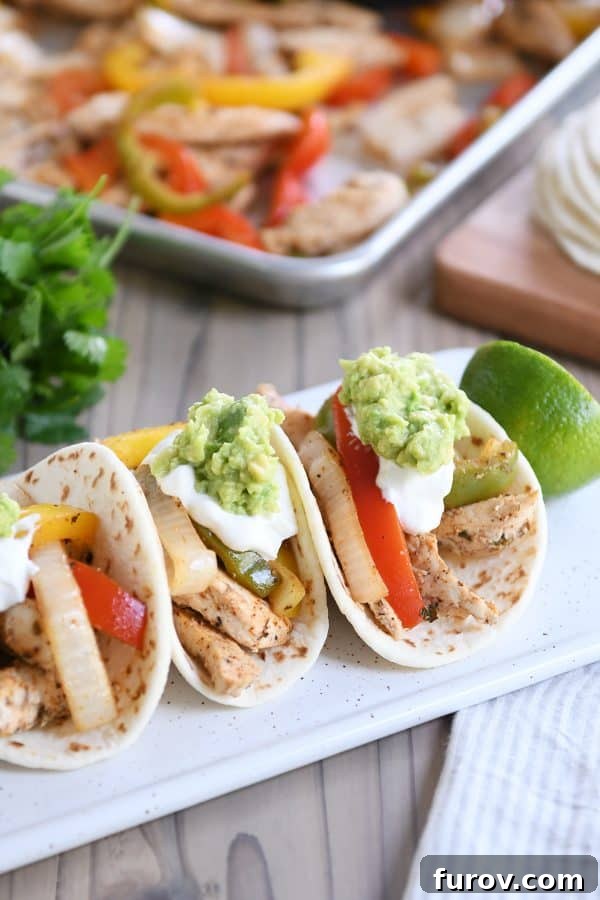 One-Pan Chicken Fajitas 3 Three perfectly cooked easy sheet pan chicken fajitas on a white board, generously topped with creamy sour cream and rich guacamole.