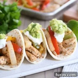 Three easy sheet pan chicken fajitas on white board topped with sour cream and guacamole.