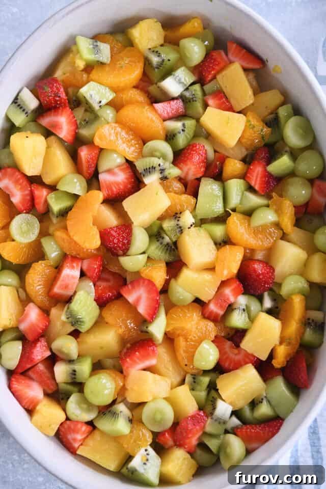 Zesty Honey Lime Fruit Medley 2 A beautifully arranged white oval serving dish filled with a colorful assortment of canned pineapple, vibrant strawberries, luscious grapes, and tangy kiwi, all ready to be tossed in a honey-lime dressing.