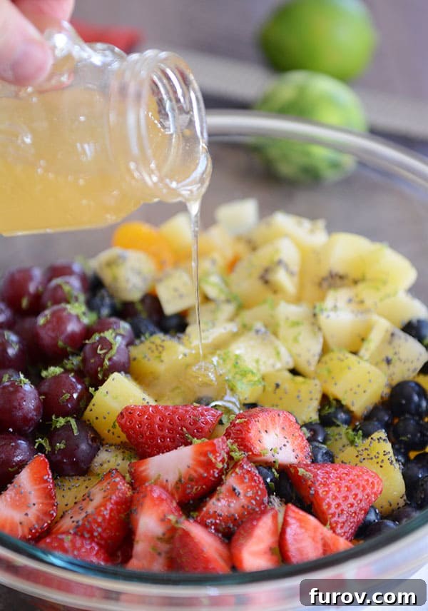 Zesty Honey Lime Fruit Medley 8 A glass bowl generously filled with perfectly chopped fresh fruit, adorned with sprinkled lime zest, as the vibrant honey-lime dressing is carefully poured over the entire mixture, creating a refreshing fruit salad.