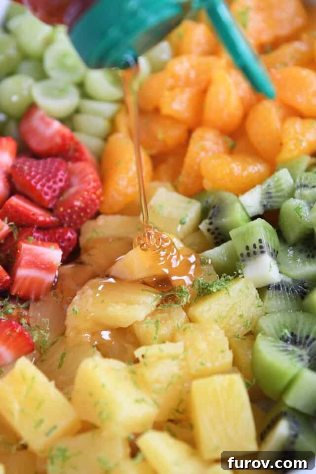Zesty Honey Lime Fruit Medley 3 Close-up shot of golden honey being generously drizzled over glistening canned pineapple chunks in a bowl, highlighting the sweet addition to the fruit salad.