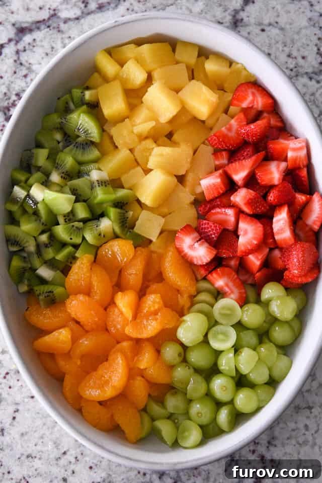 Zesty Honey Lime Fruit Medley 4 A vibrant white oval bowl showcasing a medley of fresh ingredients including halved grapes, bright mandarin oranges, sliced kiwi fruit, succulent pineapple chunks, and sweet strawberries, all meticulously prepared for a refreshing fruit salad.