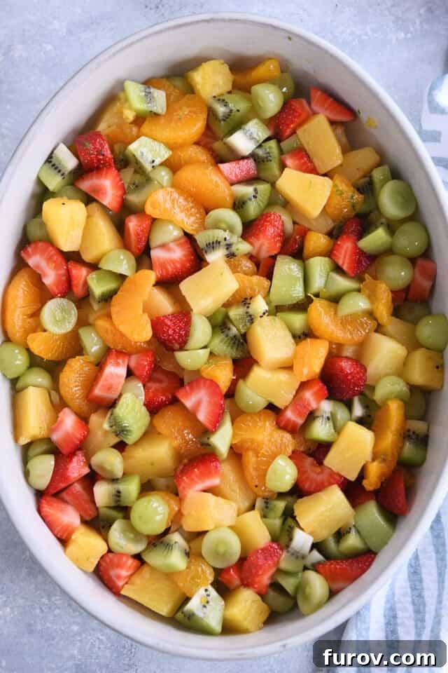 Zesty Honey Lime Fruit Medley 5 A large white oval serving dish generously filled with a vibrant and fresh assortment of strawberries, mandarin oranges, pineapple, and kiwi, beautifully arranged for serving.