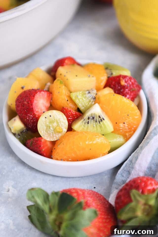Zesty Honey Lime Fruit Medley 6 A small white dish elegantly presenting a colorful mix of sliced kiwi, halved grapes, segments of mandarin oranges, and quartered strawberries, perfect for a single serving of fresh fruit salad.