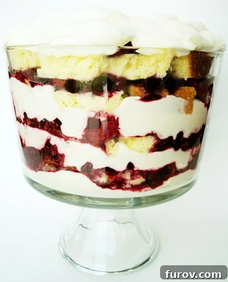 Zesty Berry Trifle 2 Clear trifle dish showcasing beautiful layers of golden lemon pound cake, vibrant mixed berries, and creamy white whipped topping, garnished with fresh berries and lemon slices.